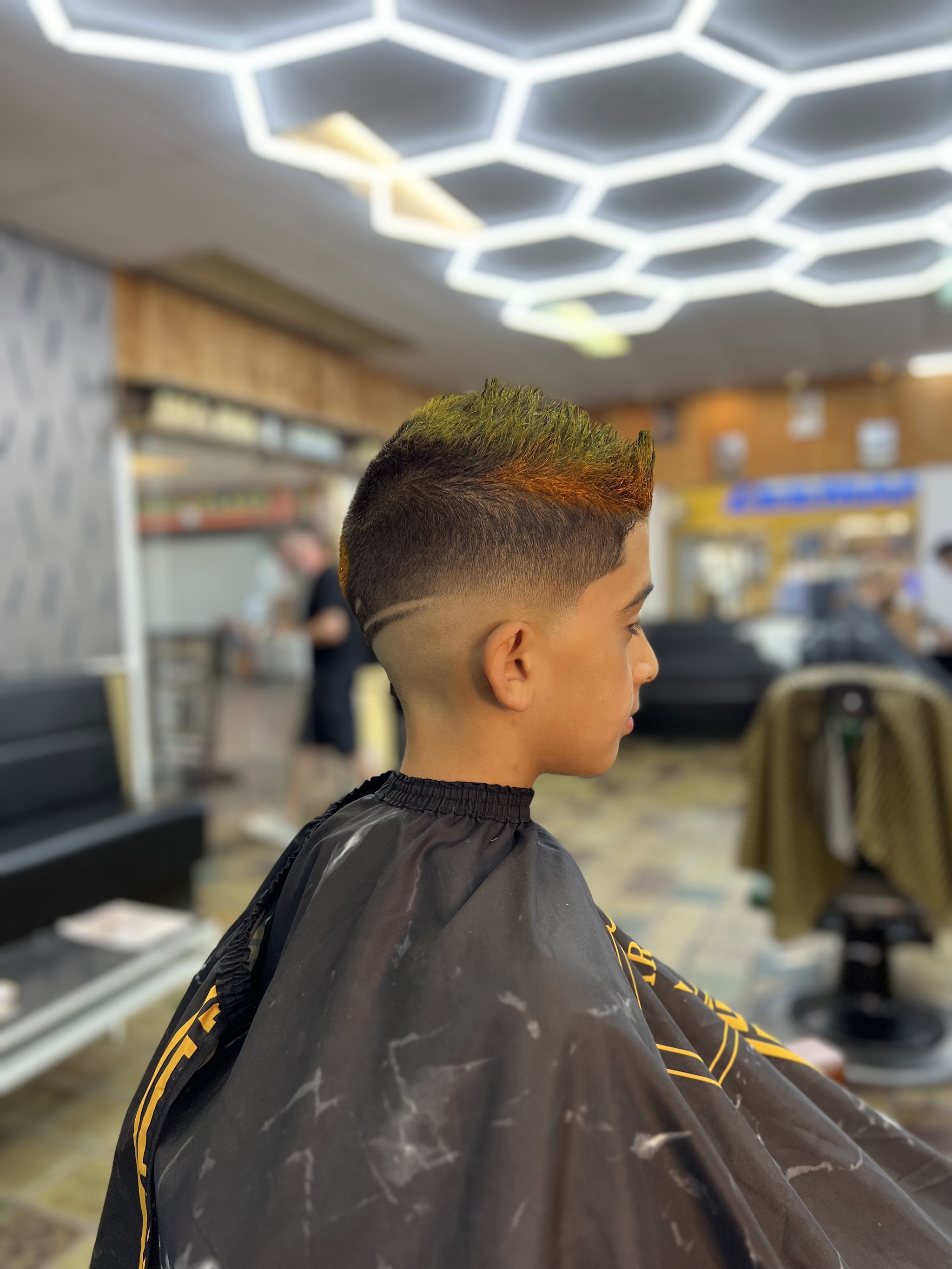 Jongen in de stoel met een fade en een gekleurde bovenkant, onder het zeshoekige plafondlicht