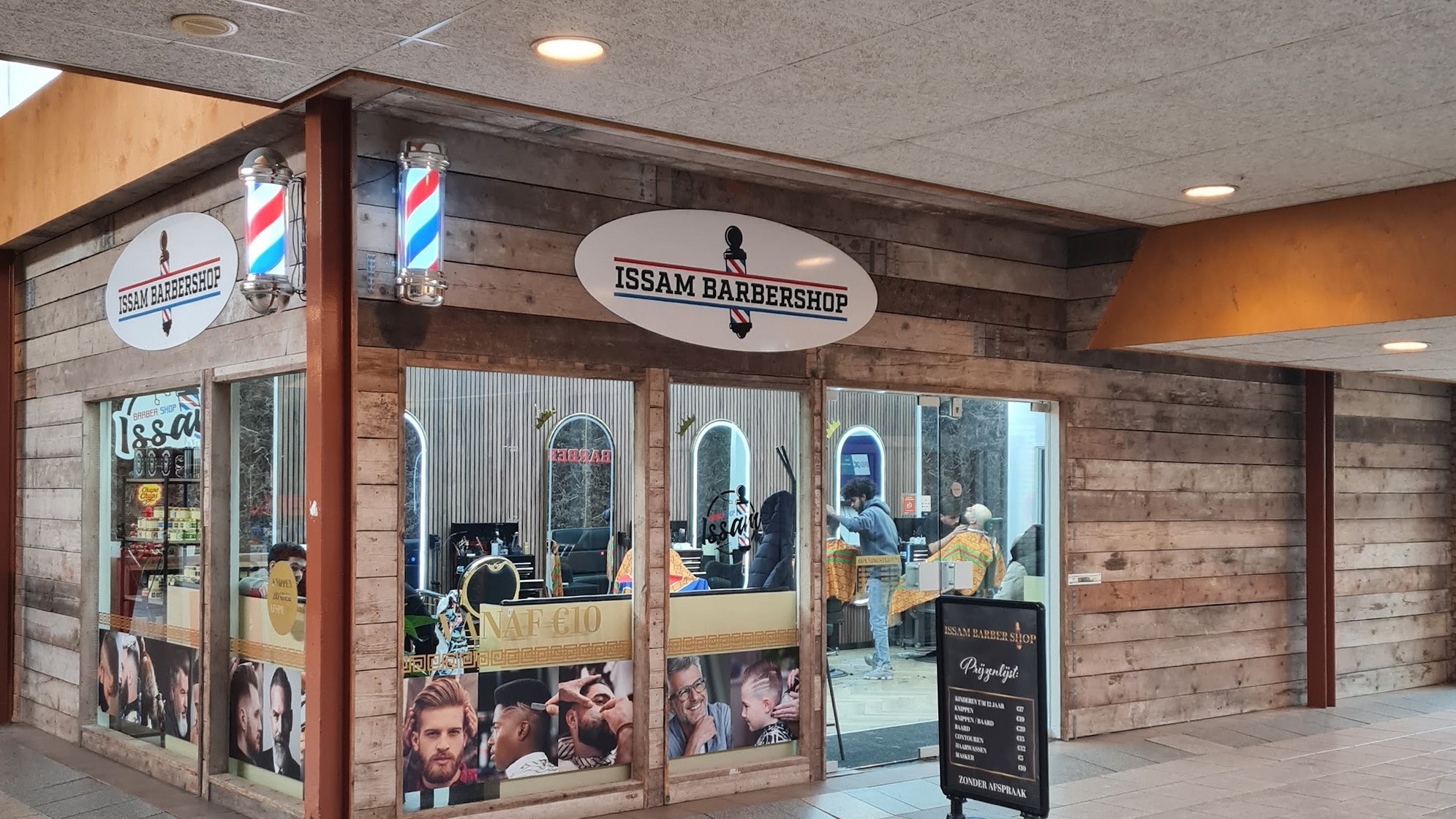De zaak van Issambarbershop in Winkelcentrum Dauwendaele, met twee kapperspalen en de ovale borden boven de ramen