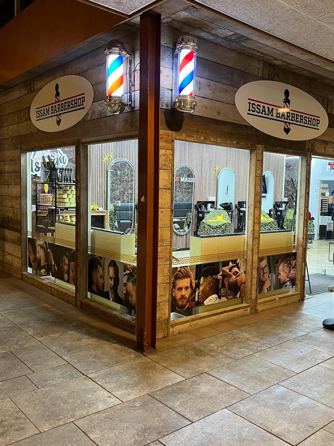 De gevel van Issambarbershop in het winkelcentrum, met de kapperspalen en de ovale borden